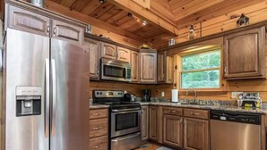A modern kitchen with stainless steel appliances, wooden cabinets, granite countertops, and a window providing natural light.