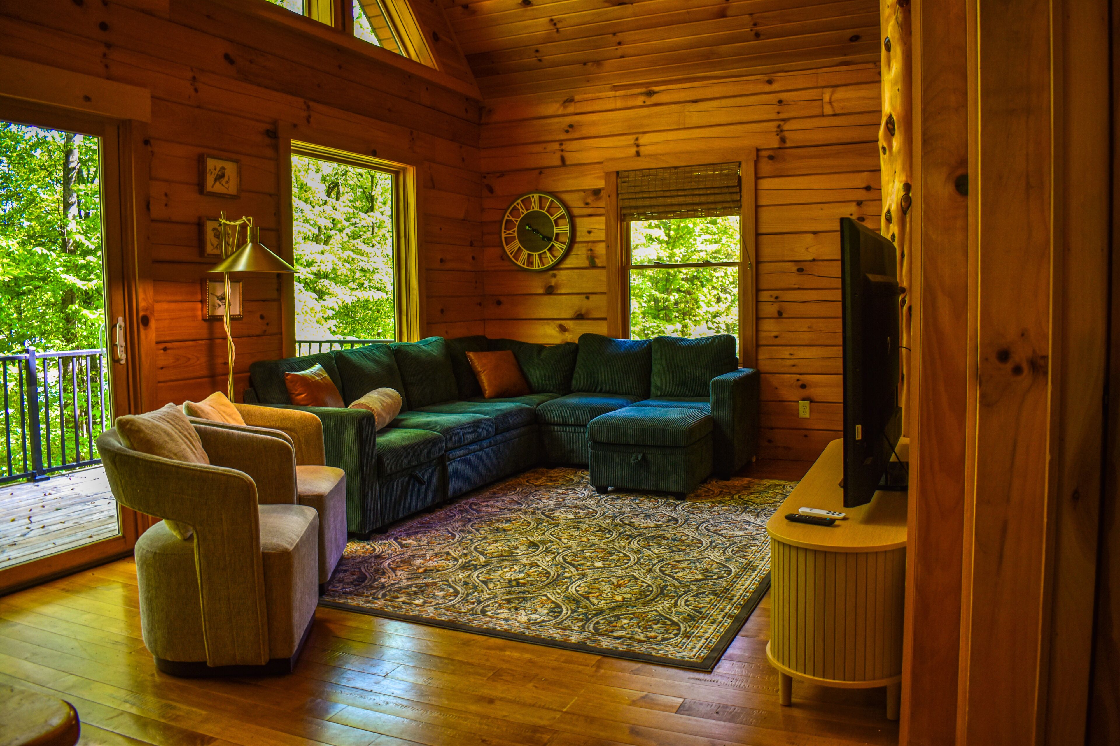 A wooden cabin interior with a sectional sofa, a small table, and a television.