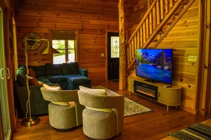 Acogedor interior de cabaña con paredes de madera, un sofá, otomanas, un televisor y una chimenea.
