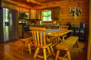 Interior de una cabaña de madera con una mesa de comedor, sillas, un refrigerador, microondas, horno y un lavaplatos.
