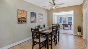 A dining area with a wooden table and chairs, a ceiling fan, and three 'New Mexico' posters on the wall.
