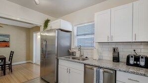 A modern kitchen with white cabinets, stainless steel appliances, a granite countertop, and a window with blinds.