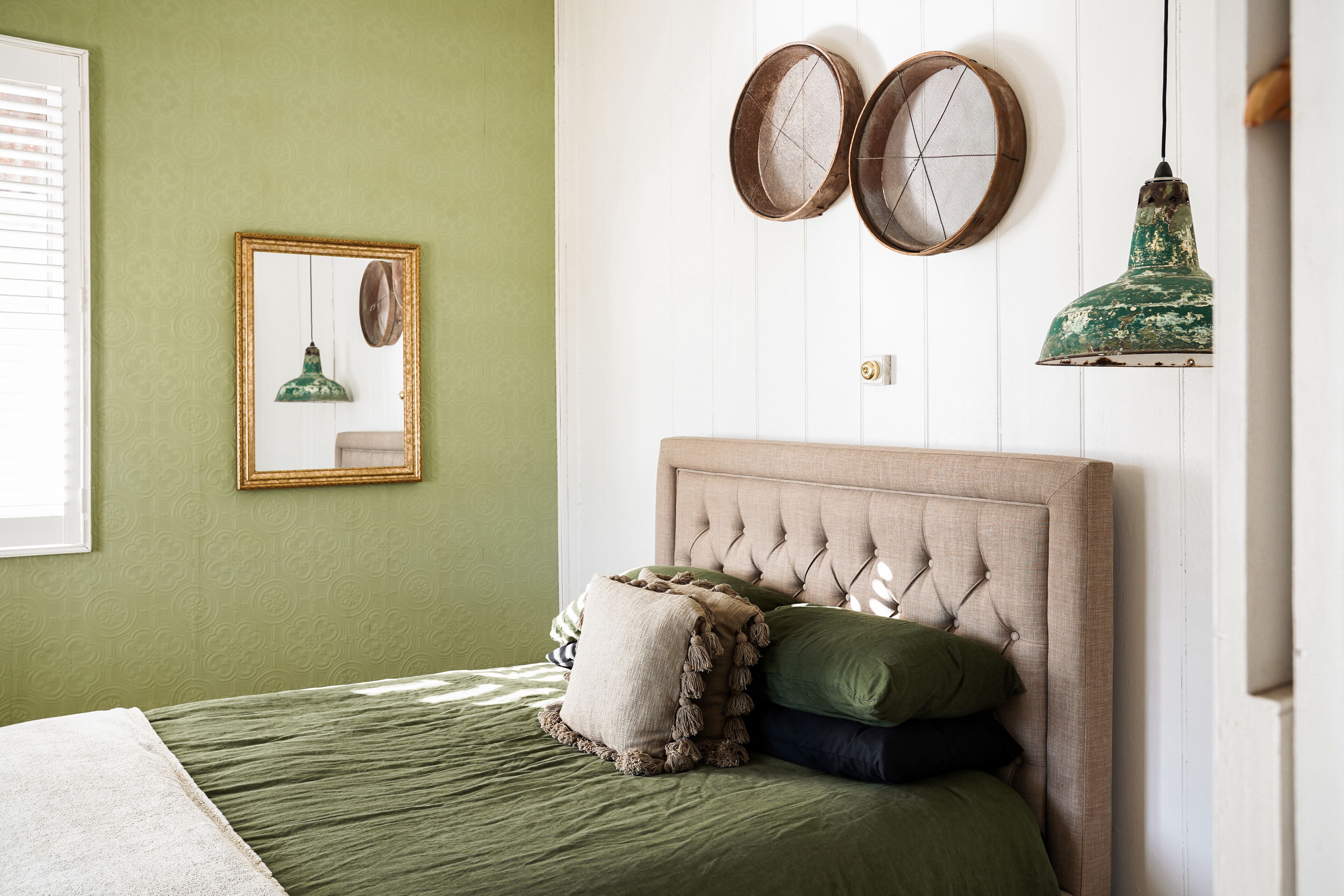 A bedroom with a green bedspread, a tufted headboard, and two round mirrors on the wall.