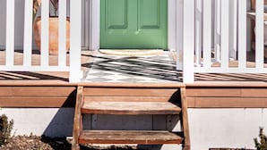 Un edificio blanco con una puerta verde, barandales blancos y una escalera de madera que conduce a la entrada.