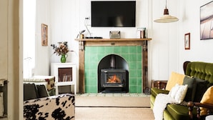 Una sala de estar acogedora con chimenea, un sofá verde, una silla de madera y un televisor montado en la pared.