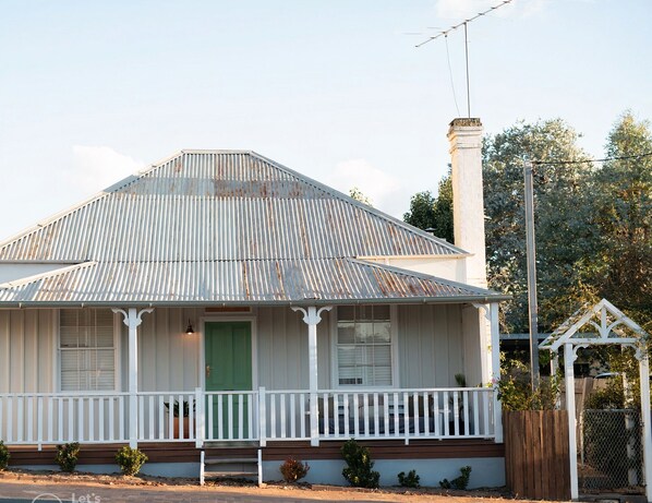A two-story house with a green door, white porch railing, and a metal roof. - Mill Cottage (Tenterfield)