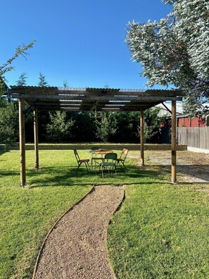 A covered patio area with a table and chairs, surrounded by a well-maintained lawn and a gravel path. - Mill Cottage (Tenterfield)