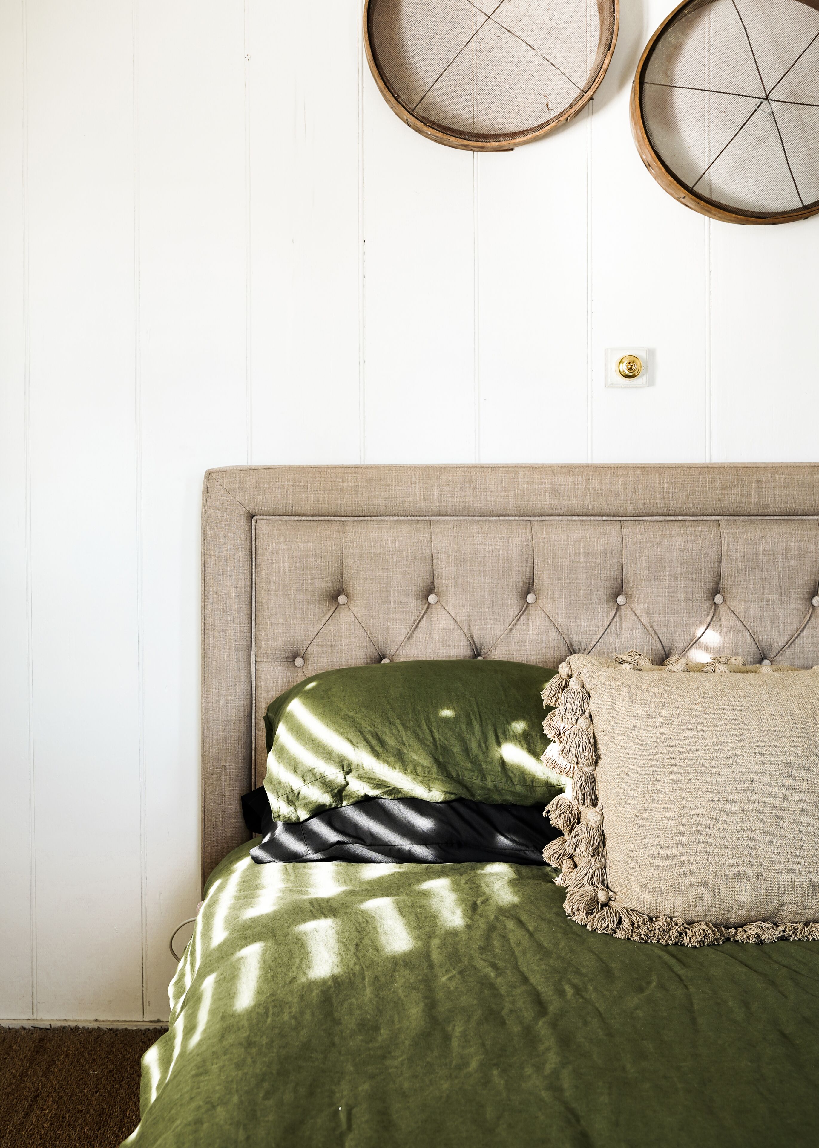 Een bed met een gestoffeerd hoofdbord, een groene spreideken en een beige kussen.