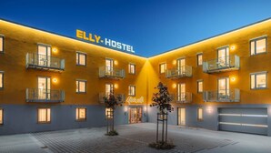 Une auberge de jeunesse à la façade jaune, dotée de nombreux balcons et d’une enseigne indiquant « ELLY HOSTEL ».