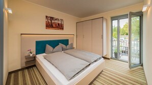 Une chambre d’hôtel avec un lit, une table de chevet, une plante en pot, une porte coulissante donnant sur un balcon et un tableau au mur.