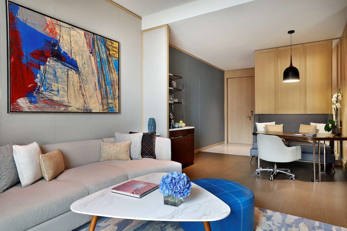 A modern living room with a sofa, coffee table, and a painting. There is a dining area with a table and chairs.