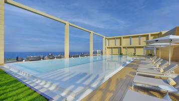 Un espace piscine avec des chaises longues et vue sur l’océan.