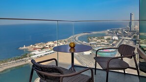 Ein Balkon mit Korbstühlen und einem kleinen Tisch, der auf einen Küsten-Stadtblick mit freiem Blick auf das Meer und die Gebäude führt.