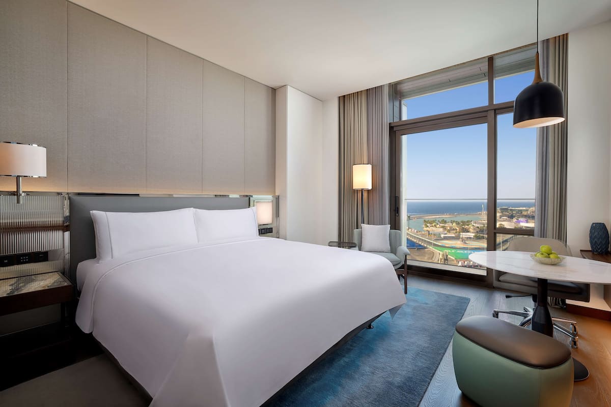 A hotel room with a large bed, a desk, a chair, and a view of the city.