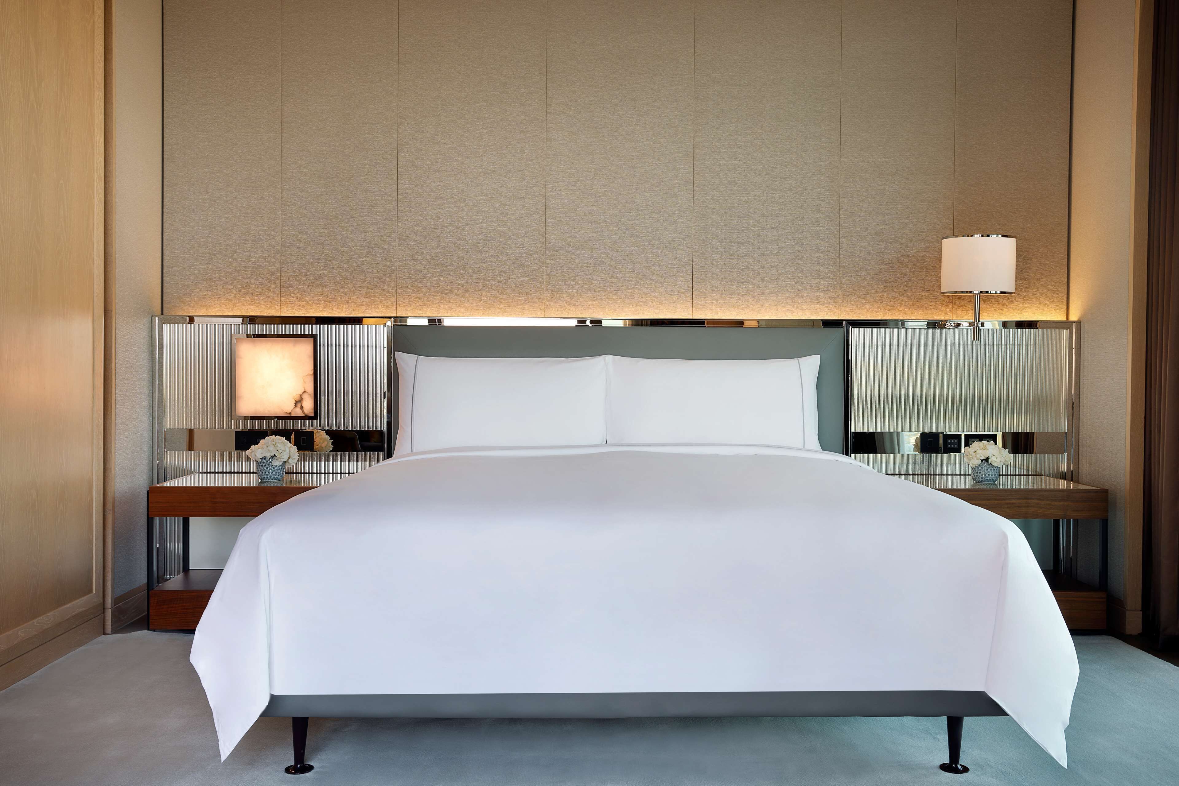 A large bed with a white bedspread, two bedside tables with lamps, and a large mirror above the bed.