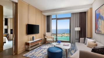 A modern hotel room with a large window, a flat-screen TV, a sofa, a coffee table, and a view of the ocean.