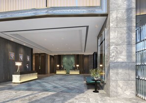 A spacious lobby with a marble floor, a reception desk, and a seating area with a green sofa.