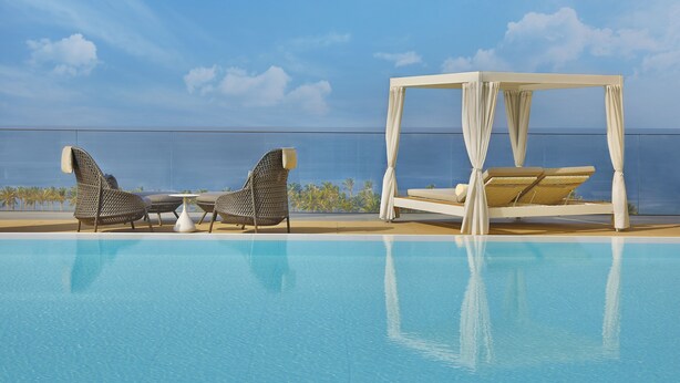 Ein Poolbereich mit einem Baldachinbett, Liegestühlen und Blick auf das Meer.