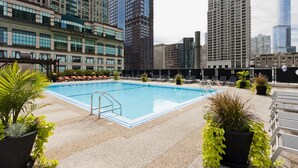 Ein Pool auf dem Dach mit Liegestühlen und Topfpflanzen, umgeben von Hochhäusern.