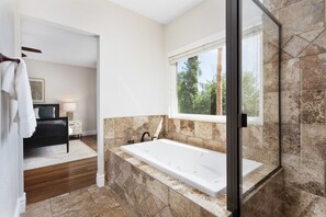 Une salle de bain moderne dotée d’une baignoire, d’un espace douche et d’une fenêtre donnant sur un paysage verdoyant.