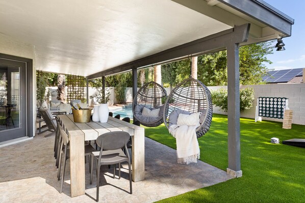 Une terrasse extérieure couverte, aménagée avec une table à manger, des chaises et des fauteuils suspendus.