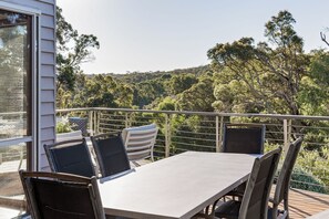 A balcony with a table and chairs, overlooking a forested area.
