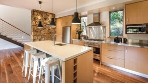 Una cocina moderna con una isla grande, armarios de madera, electrodomésticos de acero inoxidable y una pared decorativa de piedra.