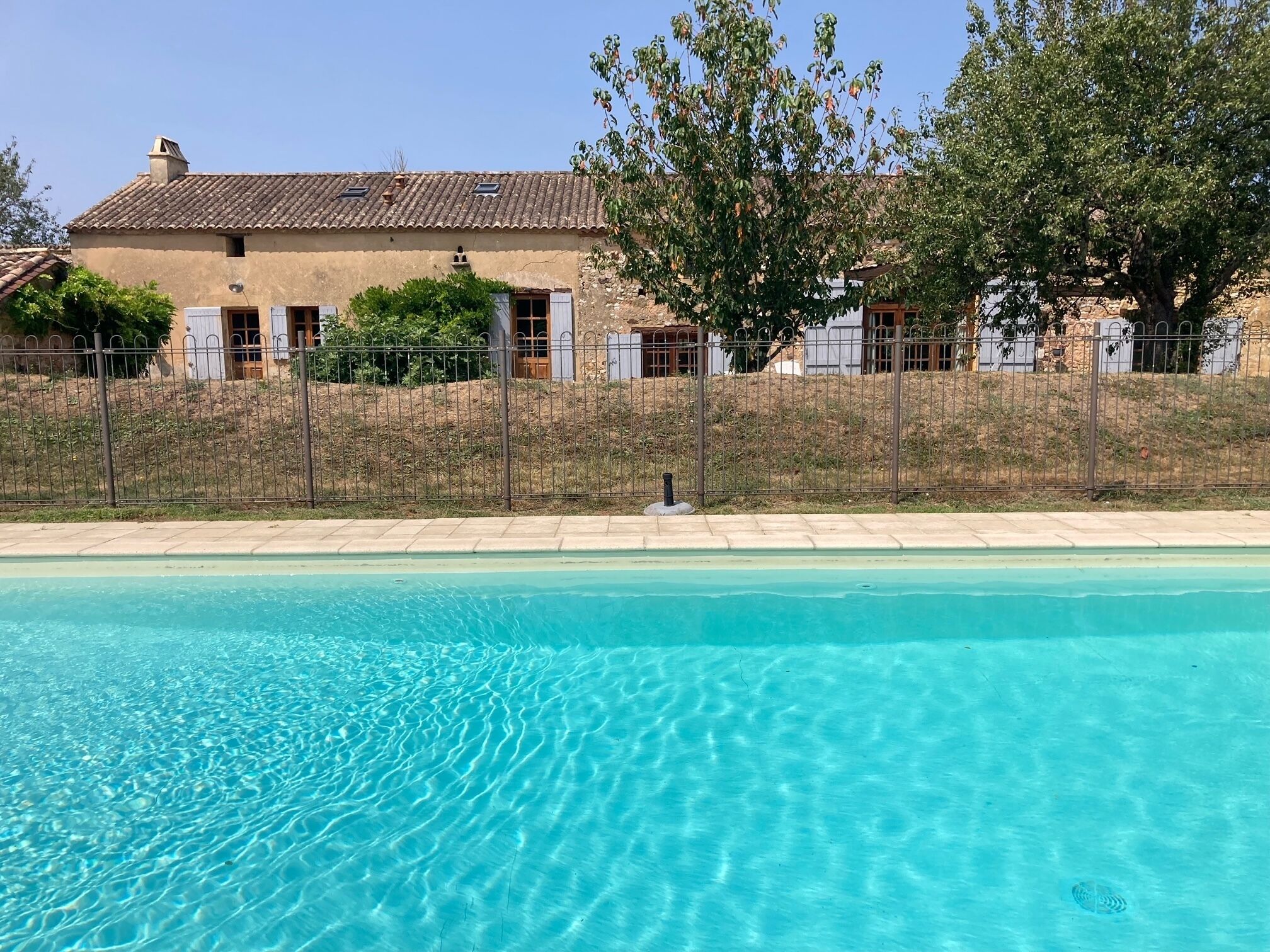 Une piscine d’eau bleue et limpide, avec une maison en arrière-plan.
