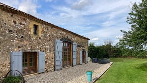Un edificio de piedra con varias ventanas y contraventanas, un camino de grava y un jardín con césped.