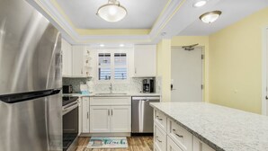 A modern kitchen with stainless steel appliances, white cabinets, and a marble countertop. - 180° Gulf Views | 1st Floor Condo| Pool & Walk to Dining (Fort Myers Beach)
