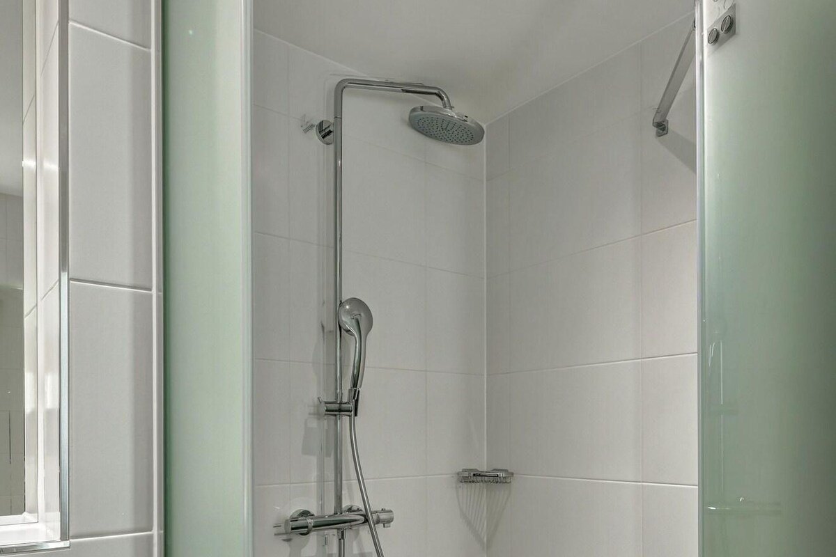 Une douche moderne dotée d’un pommeau de douche à main, d’un robinet mural et d’un espace de douche délimité par des parois en verre.