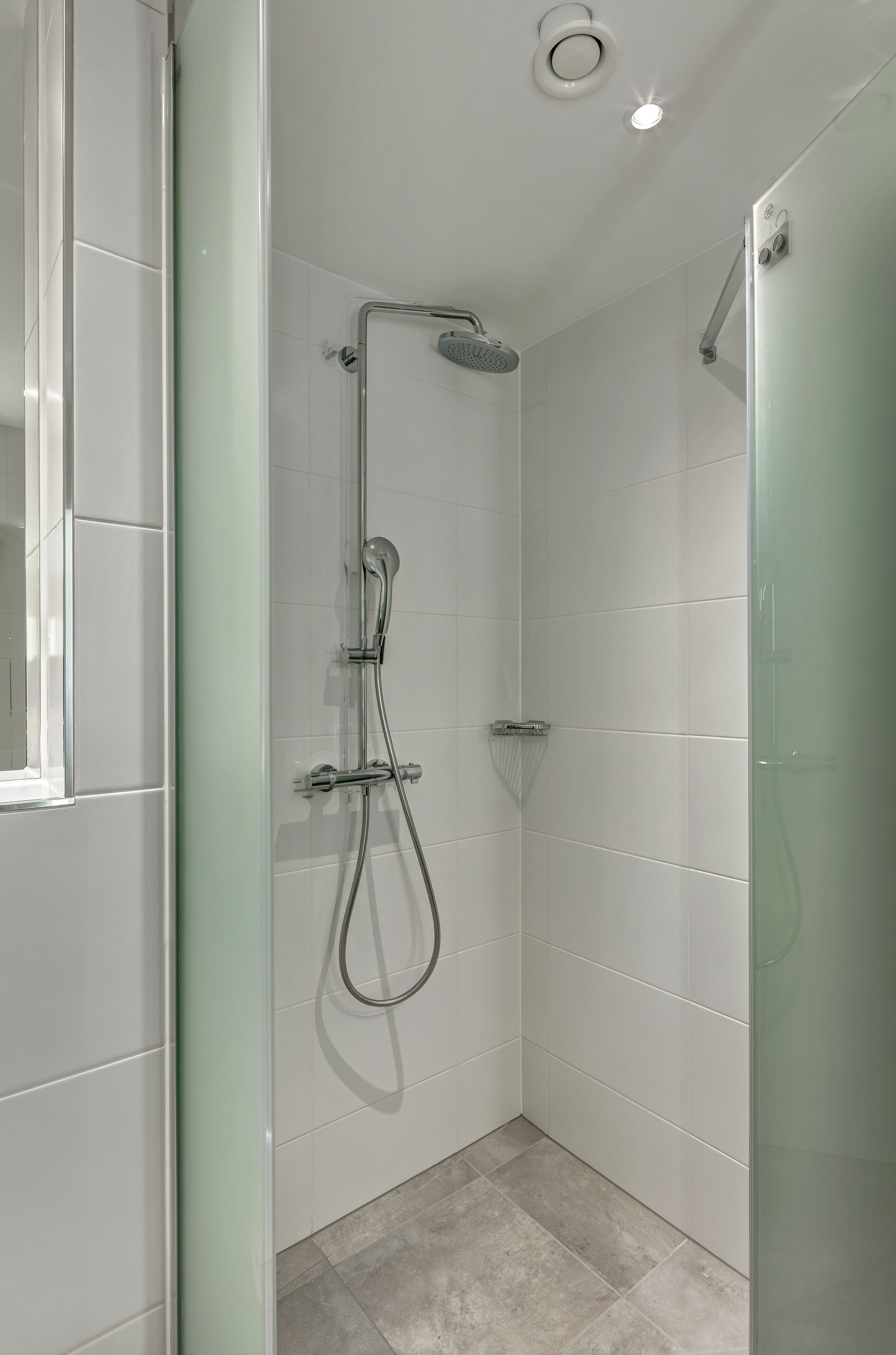 A modern shower with a glass door, a handheld showerhead, and a wall-mounted faucet.