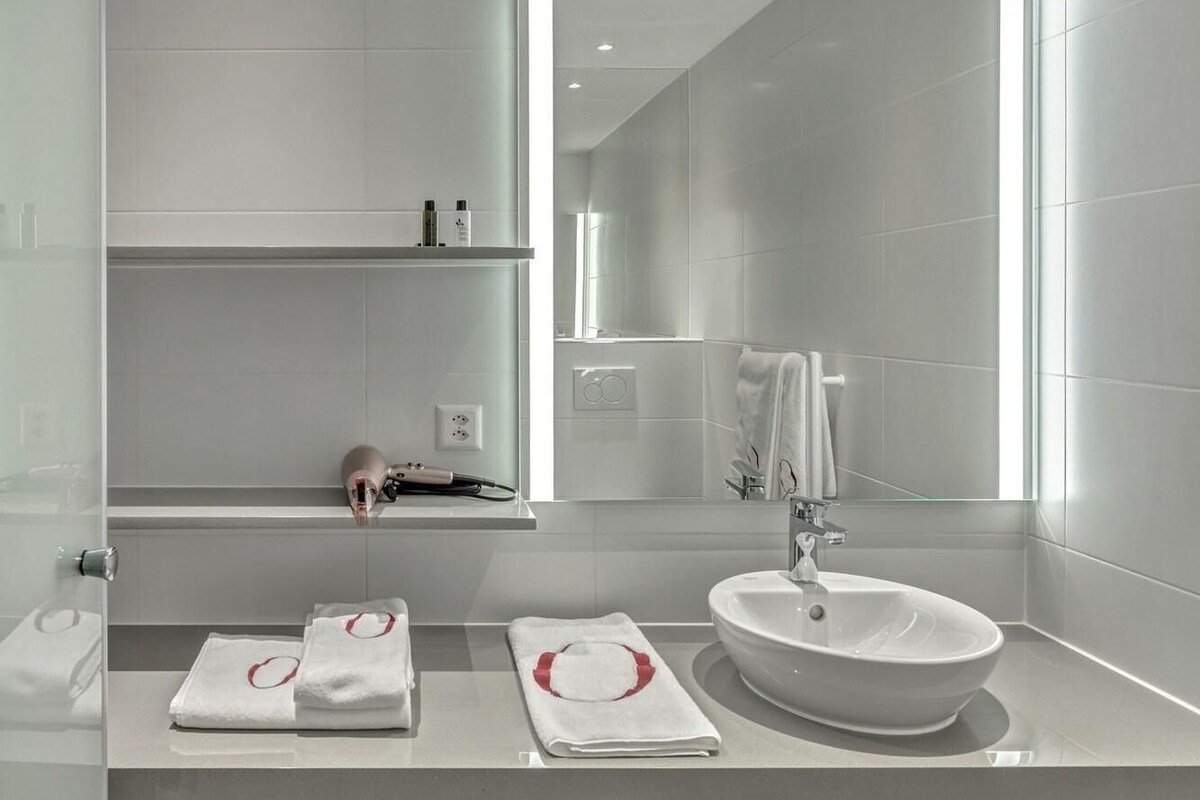 A modern bathroom with a large mirror, a sink, and two towel racks.