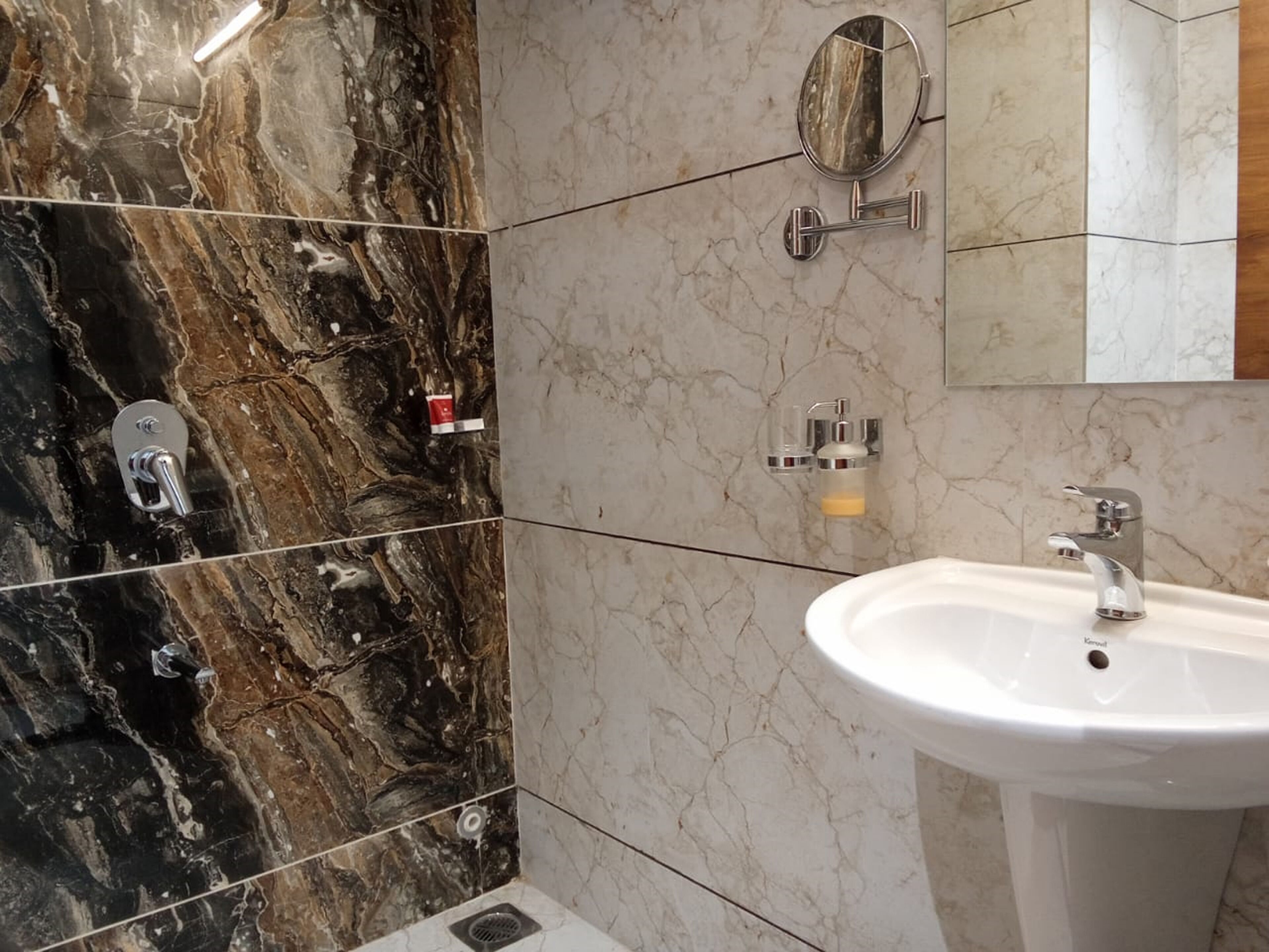 A bathroom with a marble wall, a sink, a mirror, and a shower.