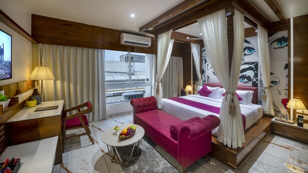 Una camera d'albergo con un letto, una scrivania, una sedia, un piccolo tavolo con della frutta e vista sull'esterno.