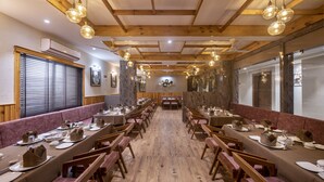 Un ristorante con travi in legno e lampade pendenti, lunghi tavoli apparecchiati per la cena, e un pavimento in legno.
