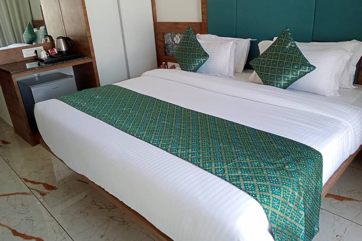 A hotel room with a large bed, a wooden headboard, a desk with a kettle, and a refrigerator.
