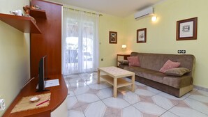 A living room with a wooden TV stand, a sofa, a small table, and a window with sheer curtains. - Apartment 372/850 (Istria - Medulin), 1500m from the beach (Medulin)