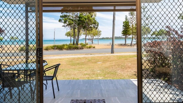 A room with a view of a beach and ocean, a table with chairs, and a welcome mat.