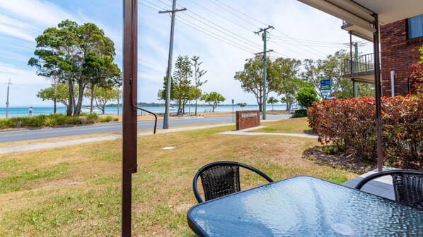 A patio with a glass table and chairs overlooking a beach and road. - Uninterruped Waterviews (BONGAREE)