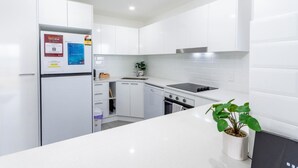 A modern kitchen with white cabinetry, a built-in oven, a sink, and a stove. There is a refrigerator with a QR code and a small plant on the counter.