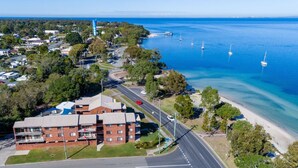 An aerial view of a coastal area with a prominent building, a road, and a beach with sailboats.
