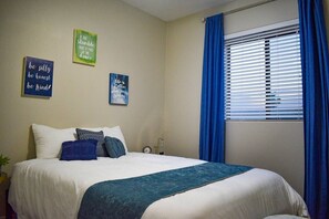 A neatly made bed with a white and blue bedspread, two pillows, and a blue throw blanket. There are three motivational wall art pieces above the bed.