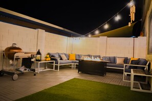 An outdoor patio with a barbecue grill, seating area, and string lights.