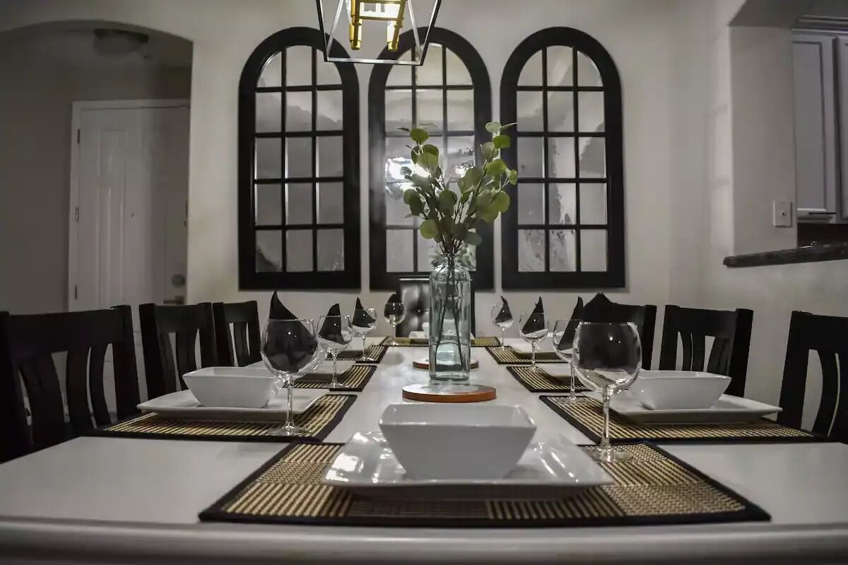 A dining table set for six with black chairs, a vase with green leaves, and a chandelier.