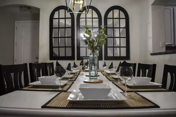 A dining table set for six with black chairs, a vase with green leaves, and a chandelier.