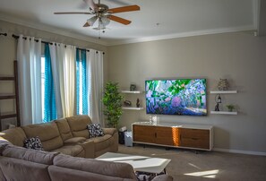 A living room with a beige sofa, a white coffee table, a TV on the wall, and a ceiling fan.