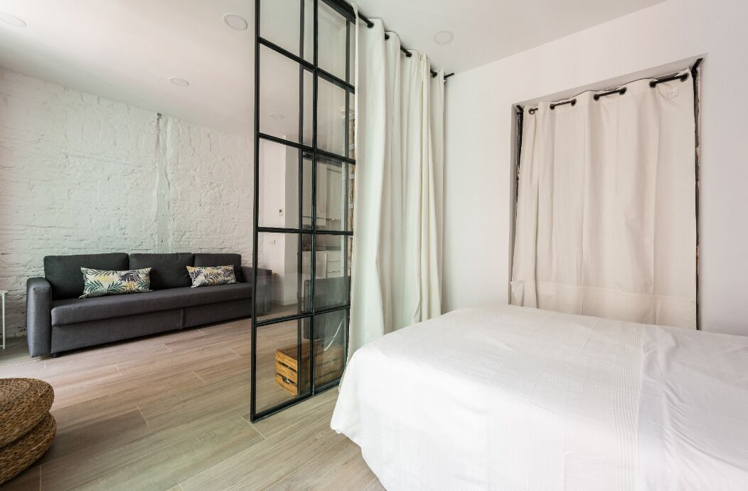 A modern bedroom with a large bed, a sofa, and a glass partition.