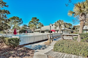 A pool area with a wooden deck, palm trees, and a white picket fence.