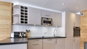 A modern kitchen with white cabinetry, a stainless steel range hood, and a built-in microwave.